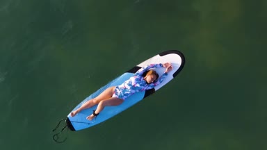 Yavaş hareket hava güzel kız beach ile okyanus dalgaları helikopter görmek bir sörf üzerinde yalan vurdu.