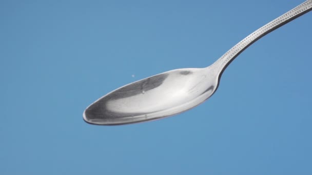 White sugar slowly fills a teaspoon and crumbles on a blue background — Stock Video
