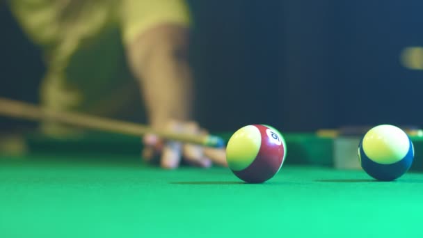 A man holds a cue, takes aim and hits a colored billiard ball. Close-up — Wideo stockowe