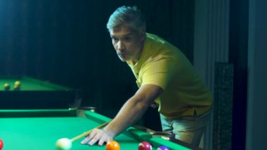 Adam bir ıstaka tutuyor, nişan alıyor ve bilardo topuna vuruyor. Bir işadamı bilardo oynar.