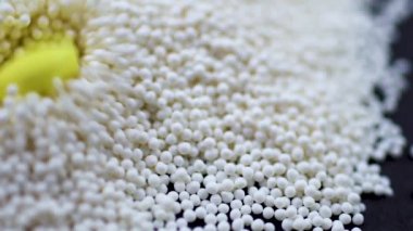 Sarı yuvarlak haplar, siyah arka plana saçılmış granüllere dökülüyor.