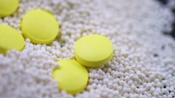 Желтые круглые таблетки, падающие в гранулы разбросаны на черном фоне крупным планом — стоковое видео