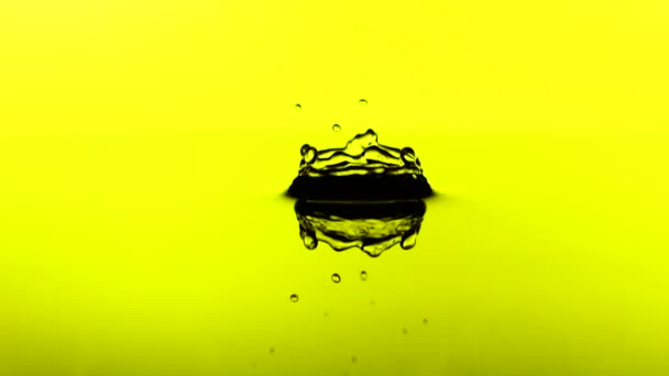 Una gota de agua cae en la superficie de un aceite en cámara lenta. Fondo amarillo . — Vídeos de Stock