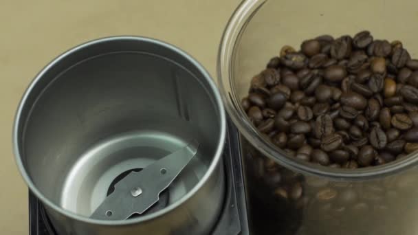 Los granos de café se vierten rápidamente en la amoladora eléctrica, fondo beige. Concepto matutino — Vídeo de stock
