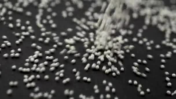 Bílé granule medicíny drolí na černém pozadí close-up zpomalení — Stock video