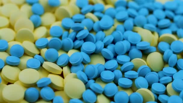 Las píldoras azules caen sobre las amarillas en la parte superior y giran sobre una mesa en una farmacia — Vídeos de Stock