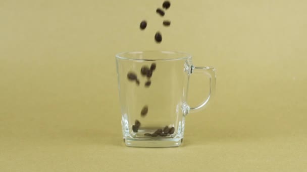 Los granos de café caen rápidamente, taza de vidrio transparente, fondo beige. Concepto matutino — Vídeos de Stock