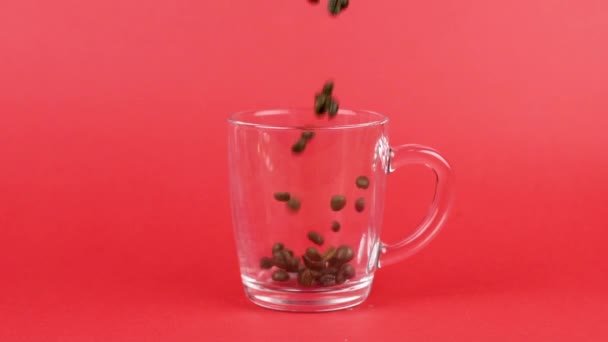 Кофейная фасоль быстро летит, перемежая стеклянную чашку, красный фон. Концепция перегрузки — стоковое видео