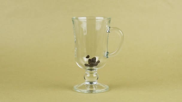 Кофейные зёрна быстро летают, прозрачная стеклянная чашка, бежевый фон. Утренняя концепция — стоковое видео