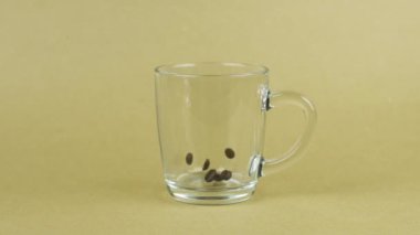 Kahve çekirdekleri çabucak düşer, cam bardak, bej arka plan. Enerji kavramı