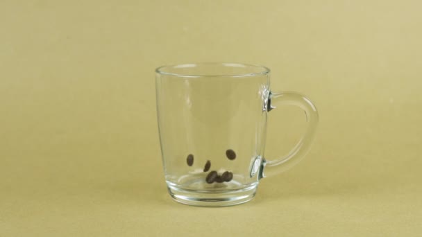 Chicchi di caffè cadono rapidamente, tazza di vetro trasparente, sfondo beige. Concetto energetico — Video Stock