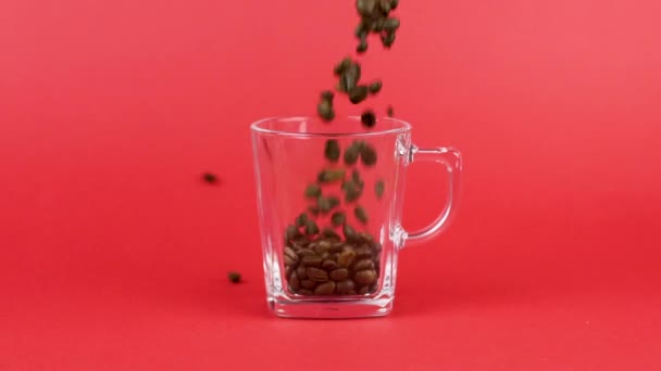 Koffiebonen snel gieten, glazen mok, rode achtergrond. Gebrek aan kracht concept — Stockvideo