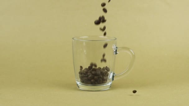 Los granos de café vuelan rápidamente, taza de vidrio transparente, fondo beige. Concepto energético — Vídeo de stock