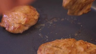 Demir bir tavada kızartılmış domuz eti. Aşçı eti yemek için maşayla çevirir..