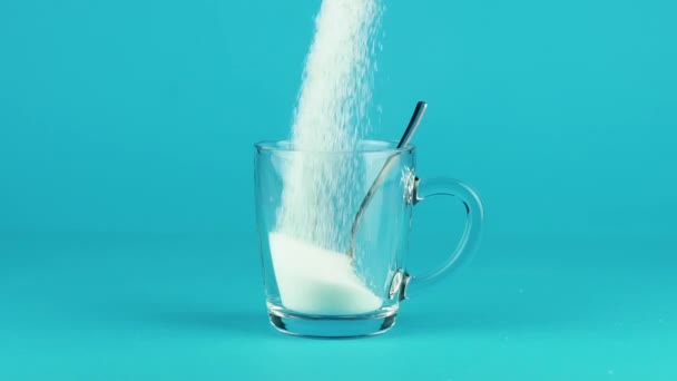 Versare zucchero tazza di vetro cucchiaino da tè blu contrasto sfondo slow motion — Video Stock