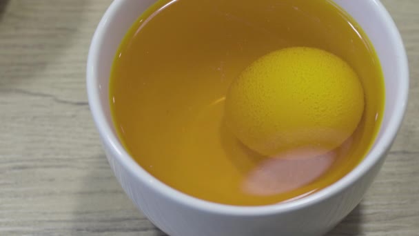 Окраска пищевых яиц желтым красителем в белой чашке на столе. Пасхальные советы по оформлению — стоковое видео
