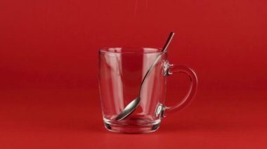 Kırmızı zıt bir arkaplanda çay kaşığıyla cam bardağa şeker dök. Kavram