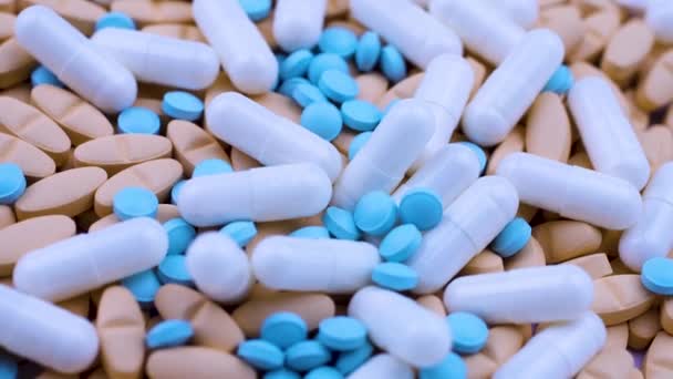 Witte capsules liggen op feloranje tabletten met kleine blauwe pijnstillers. Draaien — Stockvideo