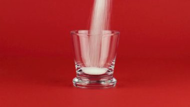 Kırmızı zıt arkaplanda kalın bir tabanı olan bir bardağa şeker dök.