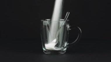 Çay kaşığı siyah zıt arkaplanlı bardak şekeri dök. Kavram