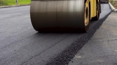 Büyük sarı bir buharlı silindir. Sıcak asfaltı düzleştirmiş. Yeni bir yol inşa eder