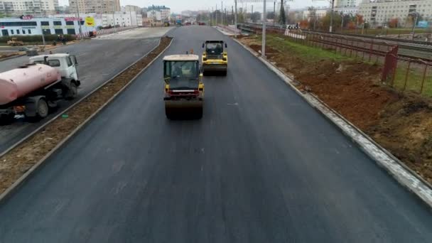 Due pavimentatori gialli cavalcano e appiattiscono l'asfalto caldo. Vapore in strada. Aerea — Video Stock