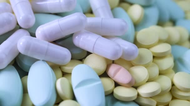 Білі капсули лежать на різнокольорових жовтих синьо-рожевих таблетках на столі крупним планом — стокове відео