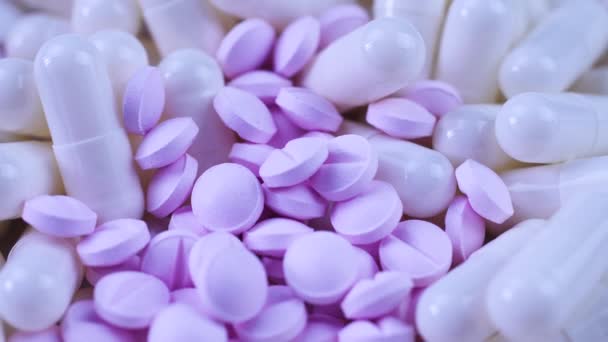 Small purple pills and white capsules lie together on a table and rotate closeup — Stock Video