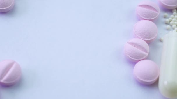 На белом столе розовые таблетки и открытая белая капсула с белыми гранулами — стоковое видео