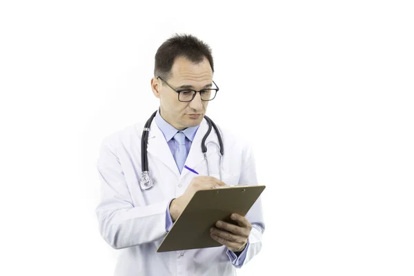 Σοβαρός ιατρός με λευκό παλτό και στηθοσκόπιο που γράφει στο πρόχειρο — Φωτογραφία Αρχείου