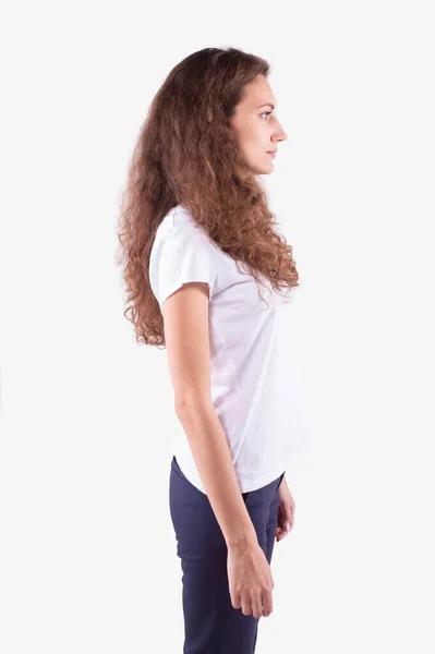 Dívka s kudrnatými vlasy stojí bokem ke kameře, dívá se před sebe. Bílé pozadí — Stock fotografie