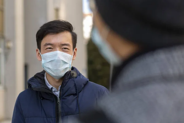 Två asiatiska unga män i medicinska skyddsmasker mot covid-2019 leenden, samtal — Stockfoto