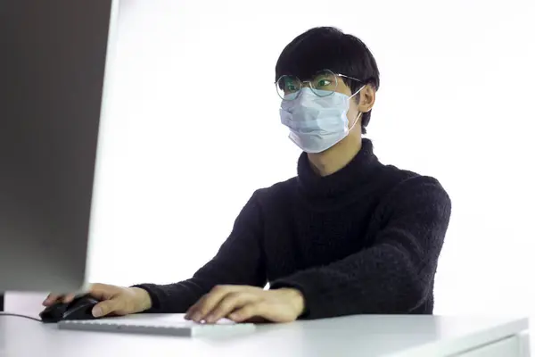 Hombre asiático en máscara quirúrgica y gafas trabajando en la oficina. Coronavirus chino —  Fotos de Stock