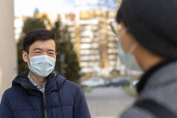 Två asiatiska män i medicinska masker mot covid-2019 ler och pratar med varandra — Stockfoto