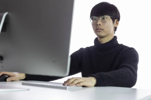 Prachtige Chinese jongeman met een bril aan die op kantoor werkt. Witte achtergrond — Stockfoto