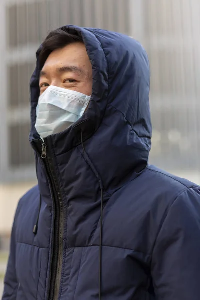 Chinese man in surgical mask against covid-2019 and hood. Outside. Quarantine