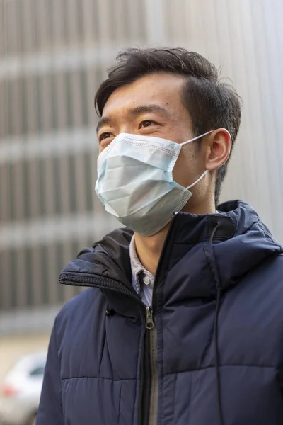 Chinese man in medical mask against 2019-nCov looking away. Outdoors