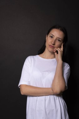 Genç bayan sakince gülümsüyor. Eller çenede. Siyah arkaplan