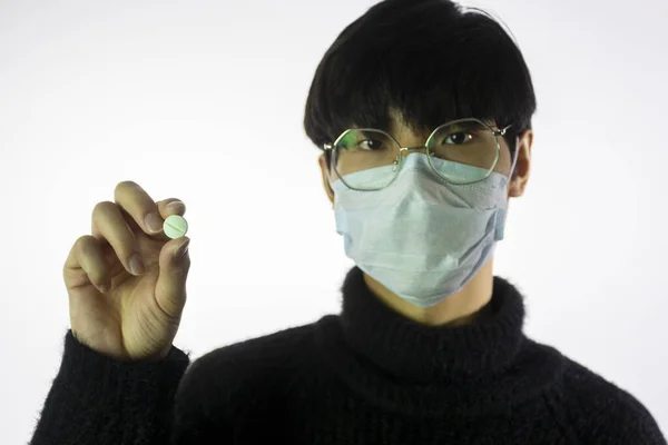 Hombre joven asiático con máscara facial, píldora en la mano. Prevenir la propagación del coronavirus —  Fotos de Stock