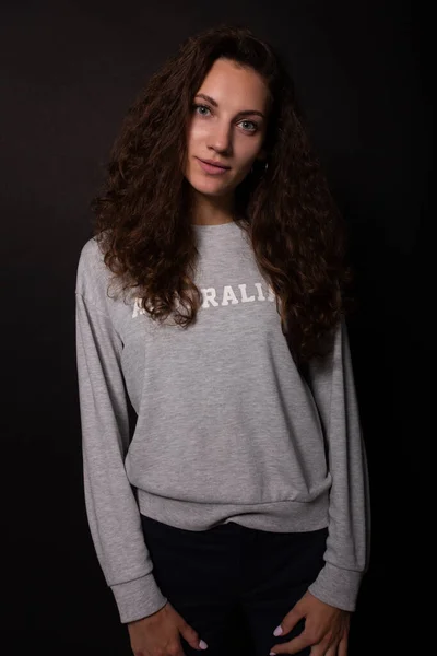 Ragazza affascinante con lunghi capelli ricci guarda la fotocamera. Fondo nero — Foto Stock