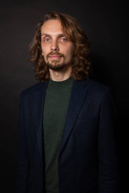 Uzun kıvırcık saçlı ve mavi gözlü olağandışı yaratıcı adam sakince kameraya bakıyor.