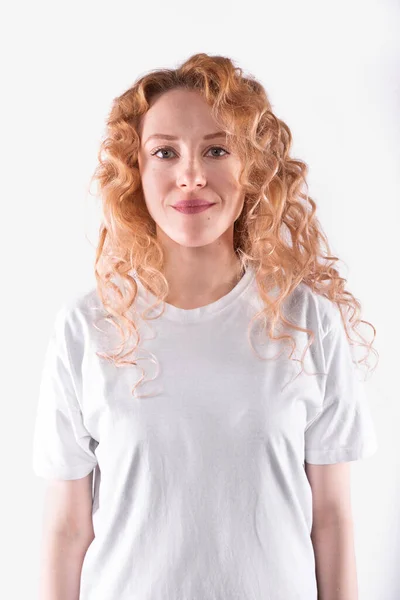 Ung kvinna med långt lockigt hår i avslappnad t-shirt söta leenden. Vit bakgrund — Stockfoto