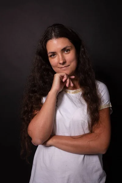 Hermosa chica adolescente que mira con calma, pequeña sonrisa. Mano en la barbilla. Fondo negro — Foto de Stock