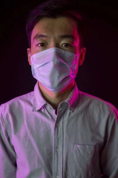 Orvosi maszkos ázsiai fiatalember portréja. Fekete háttér. Piros háttérvilágítás — Stock Fotó
