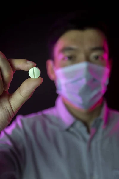 Pill in hand. Chinese man in protective mask against covid-19. Pandemic disease