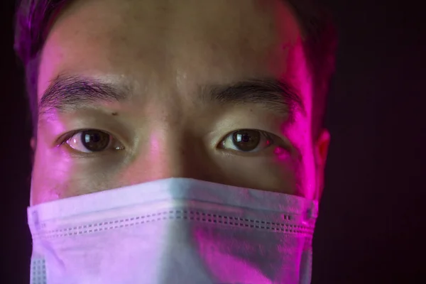 Närbild porträtt av asiatisk man i medicinsk mask mot 2019-nCov. Röd bakgrundsbelysning — Stockfoto