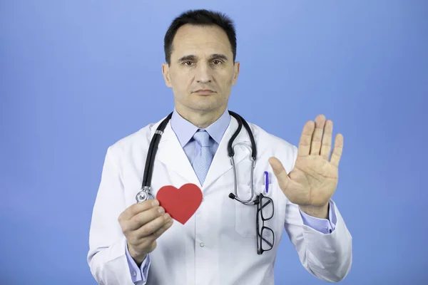 Chirurg auf hellblauem Hintergrund hält Herz in der linken Hand und zeigt rechte Handfläche — Stockfoto