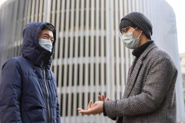 2019年，两名头戴面部医疗面具的亚洲男人对着干，互相交谈 — 图库照片