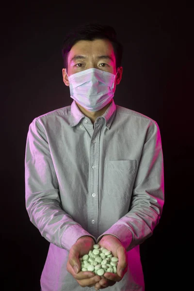 Homem asiático em máscara facial contra 2019-nCov, punhado de pílulas. Fundo preto — Fotografia de Stock