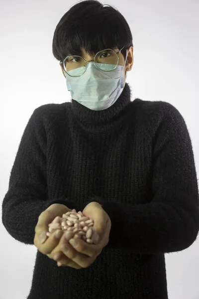 Hombre asiático con máscara médica, un puñado de pastillas. Enfermedad pandémica. Protección contra virus —  Fotos de Stock